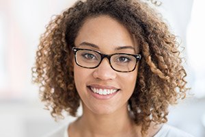 Lady with curly hair & glasses grinning after porcelain veneers