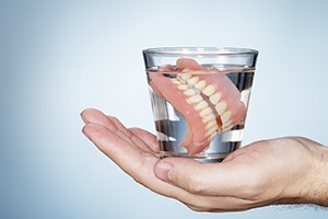 Hand holding glass of water with denture inside